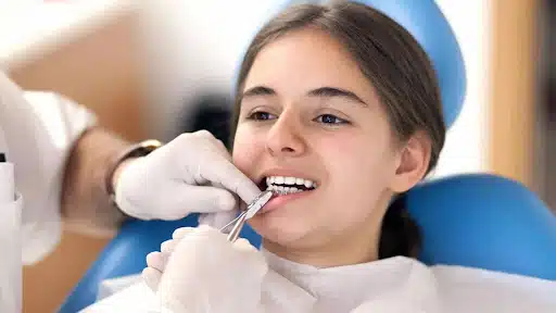 Orthodontist adjusting braces for teen patient during appointment